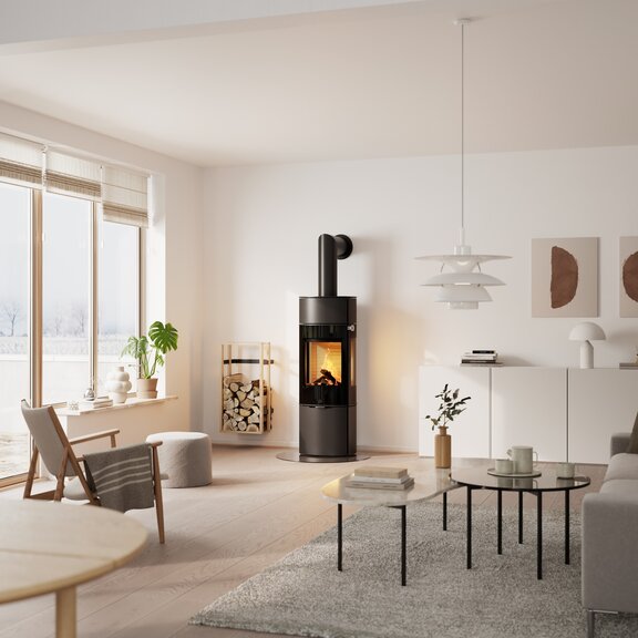 Poêle à bois CARO 130 en noir avec porte de foyer plein verre et vitre latérale dans un salon avec beaucoup de plantes