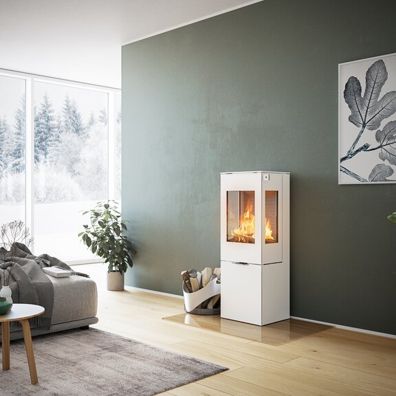 Poêle à bois NEXO 120 en blanc avec porte en acier et deux vitres latérales devant un mur vert dans un salon décoratif