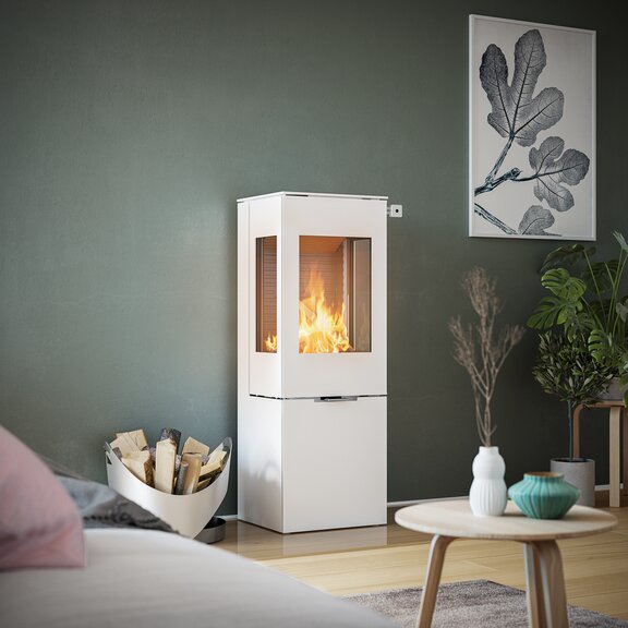 Poêle à bois NEXO 120 en blanc avec porte en acier et deux vitres latérales devant un mur vert dans un salon décoratif