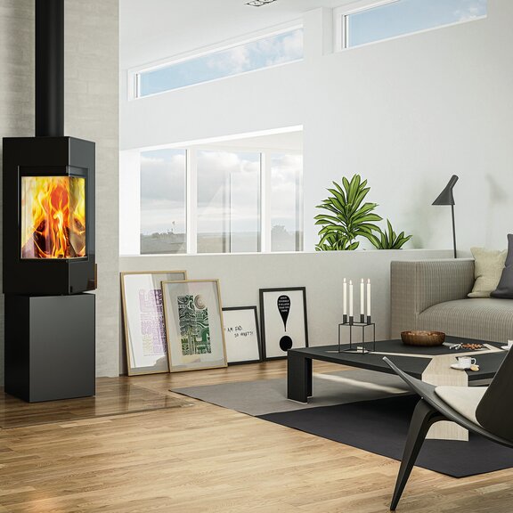 Poêle à bois Q-BE en noir avec porte en acier avec grand feu dans un appartement moderne à la campagne