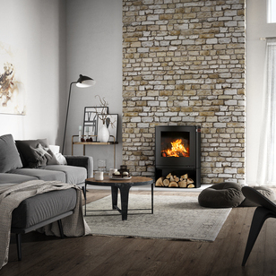 Q-TEE 2 C en noir avec compartiment à bois Poêle à bois Q-TEE 2 C en noir avec compartiment à bois dans sa forme légèrement ovale comme foyer dans une maison de campagne rustique